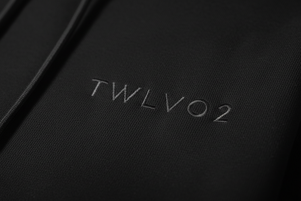 Close-up of embroidered TWLV02 logo on black hoodie fabric