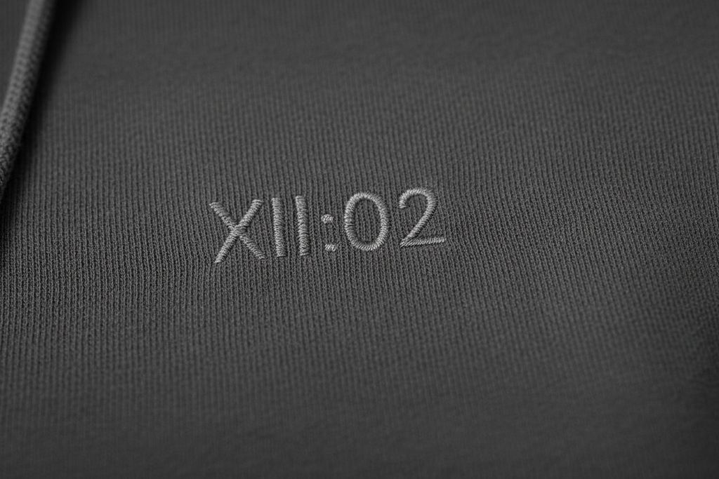 Text 'XII:02' embroidered on a dark fabric surface